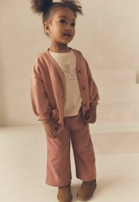 Lyserød cardigan med ballonærmer, parret med en matchende lyserød T-shirt og brede bukser. Brune ankelstøvler fuldender outfittet.