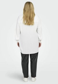 Camicia bianca a maniche lunghe con tessuto testurizzato, abbinata a pantaloni in ecopelle neri. Il look è completato da sneakers bianche.