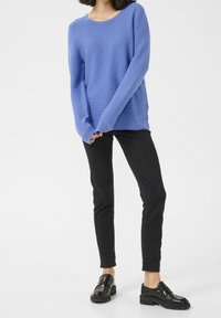 Suéter de canalé azul claro con mangas largas, combinado con pantalones negros ajustados y mocasines negros brillantes. Diseño simple y moderno.