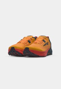 Chaussures de trail avec une tige en maille orange vif, des accents noirs et rouges, une semelle en caoutchouc durable avec une adhérence texturée, et un soutien renforcé au niveau du talon.