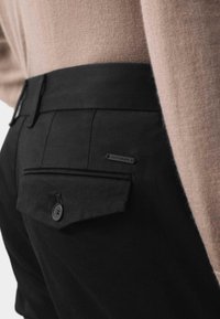 Czarne spodnie mają tylną kieszeń z zamkiem błyskawicznym i guzikiem oraz małą metkę z napisem 'AUTOGRAPH'. Tekstura jest gładka, a krój dopasowany.