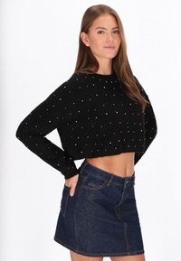 Maglione corto nero con motivi a pois colorati; abbinato a una mini gonna di jeans con tasche e chiusura con zip.