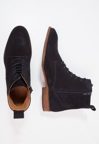 Stivaletti neri in suede con lacci davanti e zip laterale. La suola è marrone chiaro, che si abbina alla fodera interna testurizzata.