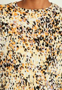 Multikleurige stof met een abstracte print in oranje, zwart en lavendel. Zachte textuur, ronde halslijn en korte mouwen.