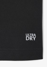 Tela negra con tejido texturizado. Logo blanco "ULTRA DRY" impreso en la esquina inferior derecha. Bordes limpios con costuras mínimas visibles.