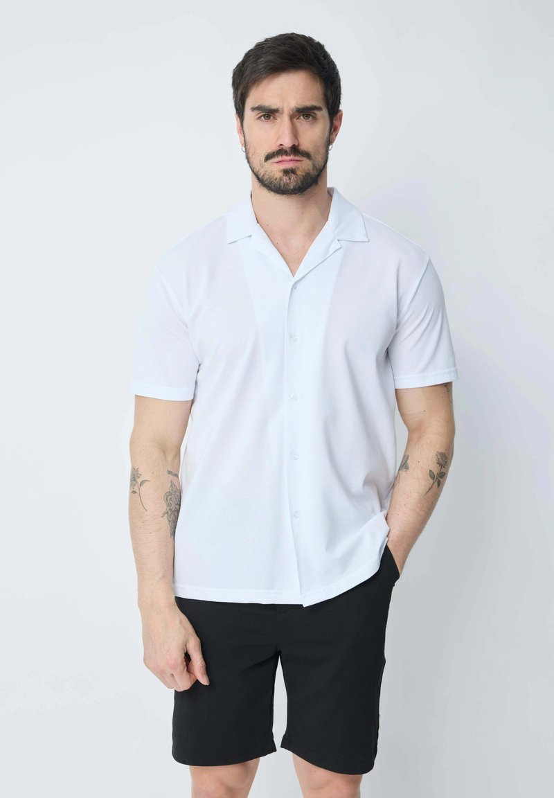 Chemise blanche à manches courtes avec col camp, associée à un short noir. Tissu lisse avec un design uni, sans motifs ni accents.