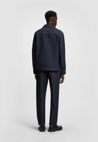 Denimjakke med lige snit, mørkeblå farve, lange ærmer, knaplukning ved håndleddene og rygdetalje, parret med matchende mørke denimbukser.