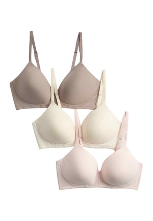 Woman with voluminous curly hair wearing a pale pink bra and a blue denim jacket slightly off her shoulders against a plain background.