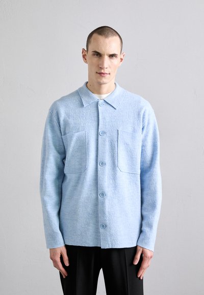 Veste chemise texturée bleu clair, dotée d'une fermeture bouton, d'un col et de deux poches poitrine, fabriquée dans un tissu doux.