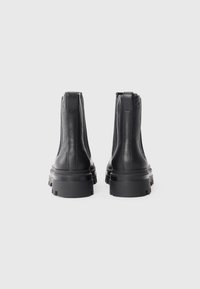 Bottes noires en cuir au niveau de la cheville avec une surface texturée, semelles en caoutchouc épaisses et languettes à l'arrière. Présente un design minimaliste et une construction robuste.