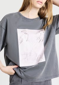 T-shirt en coton gris à manches courtes, doté d'un graphique à l'avant représentant deux danseuses de ballet esquissées dans des tons rose doux. Coupe décontractée.