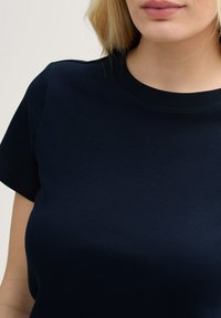 T-shirt navy blu con maniche corte, collo tondo e texture liscia, che presenta un design semplice e classico.