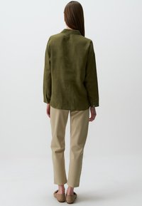 Olive green, długi rękaw, lekka lniana koszula z kołnierzykiem, w parze z beżowymi spodniami tapered i jasnobeżowymi butami wsuwanymi.