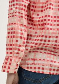 Langärmliges Hemd in rot und pink mit kariertem Muster, aus leichtem Stoff gefertigt. Es verfügt über einen geknöpften Ärmel und eine weiche Textur mit kontrastierenden hellen Quadraten.