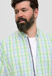 Koszula w kratę w kolorach zielonym, niebieskim i białym z kołnierzykiem zapinanym na guziki, lekkiego materiału i kontrastowym wykończeniem kołnierza. Nosi się ją na białym t-shircie.