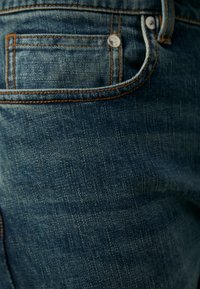 Mörkblå denimjeans har en bakficka med orange sömnad, en silvernita och en subtilt texturerad yta.