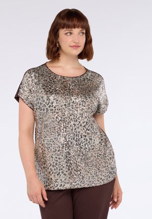 Top con lentejuelas que presenta un patrón metálico en oro y plata, de mangas cortas y cuello redondo, combinado con pantalones marrones. Textura suave.