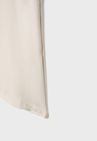 Beige stof med en lige søm, der løber lodret nær kanten, viser tekstur og lette folder på en lys baggrund.