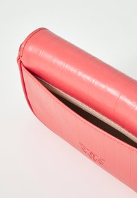 Coral-colored leather clutch bag with a textured, crocodile-like pattern. Smooth finish, open top, and subtle interior lining visible.