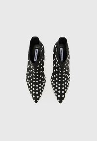 Black ankle boots with pointed toes, textured surface, and large white polka dots. Features elastic side panels for easy wear.