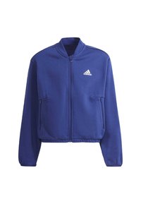 Violet zip-up takki, joka on valmistettu pehmeästä kankaasta, jossa on seisova kaulus, kaksi sivutaskua ja pieni valkoinen logo rinnassa.