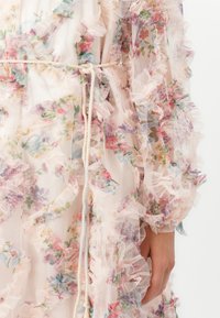 Genomskinlig blommig kimono i ljusrosa, med volanger längs kanterna, knuten med ett krämfärgat repbälte. Fina, livfulla blommönster överallt.