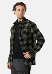 Groene en zwarte geblokte flanellen overhemd met een knoopsluiting op de kraag, een enkele borstzak en lange mouwen over een zwart shirt.