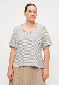 Stripet kortermet V-hals T-skjorte i lys beige med marineblå striper. Myk stoff; avslappet passform. Liten logo på venstre arm.