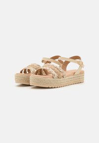 Sandalias de plataforma de punta abierta con parte superior de tejido trenzado, tiras en tono beige claro y suela de yute natural texturizado. Detalle de hebilla ajustable en el tobillo.