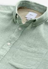 Green button-up shirt with a textured fabric, featuring a single chest pocket and a patterned inner collar. Brand label shown.