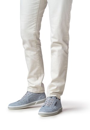 Graue Textilsneaker mit strukturierter Oberfläche, Schnürdesign und Gummisohlen. Kombination mit enganliegenden weißen Hosen.