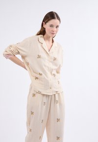 Conjunto de pijama de algodón con un patrón a rayas en beige claro y bordado floral. La parte superior de botón tiene cuello y bolsillo; pantalones holgados.