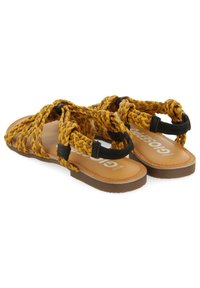 Sandalias sintéticas amarillas trenzadas con suela de goma marrón. Dos correas ajustables negras a los lados. Diseño plano, estilo abierto por delante.