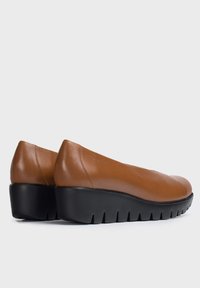 Zapatos marrones de cuero tipo slip-on con un diseño de punta redondeada y una suela negra en cuña que presenta un patrón de textura.