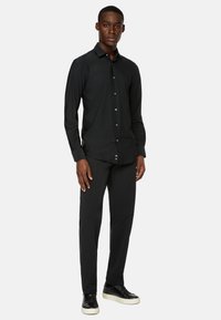 Svart långärmad skjorta med knapp-ner krage, med en slim fit-design, kombinerad med svarta skräddarsydda byxor och svarta sneakers.