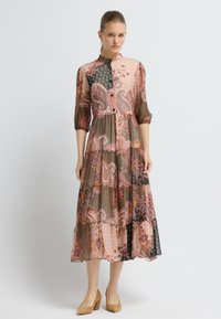 Dlouhá, vrstvená šaty s kombinací paisley a geometrických vzorů v růžových, černých a hnědých tónech. Zapínání na knoflíky, rukávy tři čtvrtě.