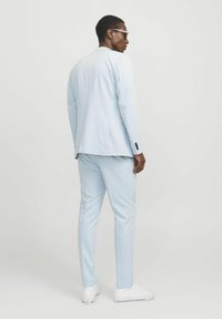 Traje azul claro compuesto por una chaqueta a medida y pantalones slim-fit, combinado con zapatillas blancas, mostrado desde atrás con gafas de sol.