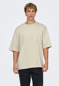 T-shirt beige oversize à manches courtes, fabriqué en coton doux, porté par un mannequin sur un fond uni.