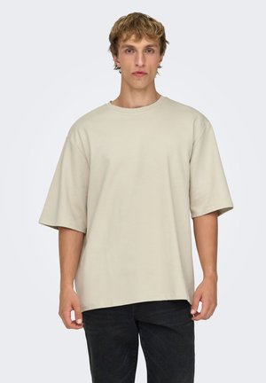 Beżowy oversize'owy t-shirt z krótkimi rękawami, wykonany z miękkiej bawełny, prezentowany na modelce na jednolitym tle.