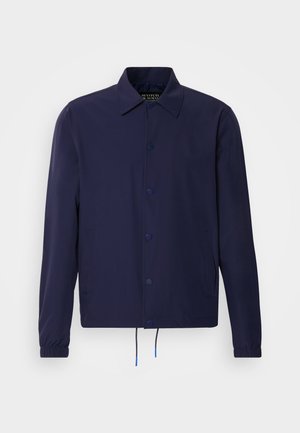 Veste coupe-vent bleu marine avec un col, des boutons pression à l'avant, des poignets élastiques et un ourlet à cordon de serrage. Elle comporte des poches latérales.