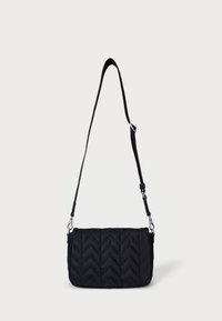 Črna prešita torba za čez ramenski trak s chevron vzorcem, ki ima odsevni ramenski trak in srebrno-tonirano kovinsko opremo. Teksturan zaključek tkanine.