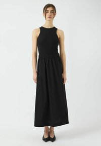 Haut noir sans manches avec un corsage ajusté, associé à une jupe noire à jambes larges avec une taille élastique. Tissu texturé, design minimaliste.