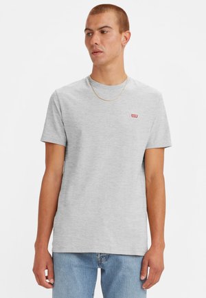 Camiseta de algodón gris con cuello redondo, mangas cortas y un pequeño logo rojo de Levi's en el lado izquierdo del pecho. Combinada con unos jeans de color azul claro.