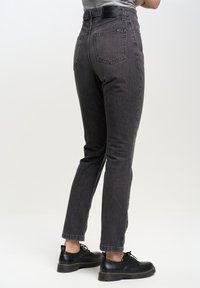 Jeans en denim gris avec une coupe slim, cinq poches et des coutures contrastées. Dotés d'une taille haute et de poignets retroussés. Associés à des chaussures noires.