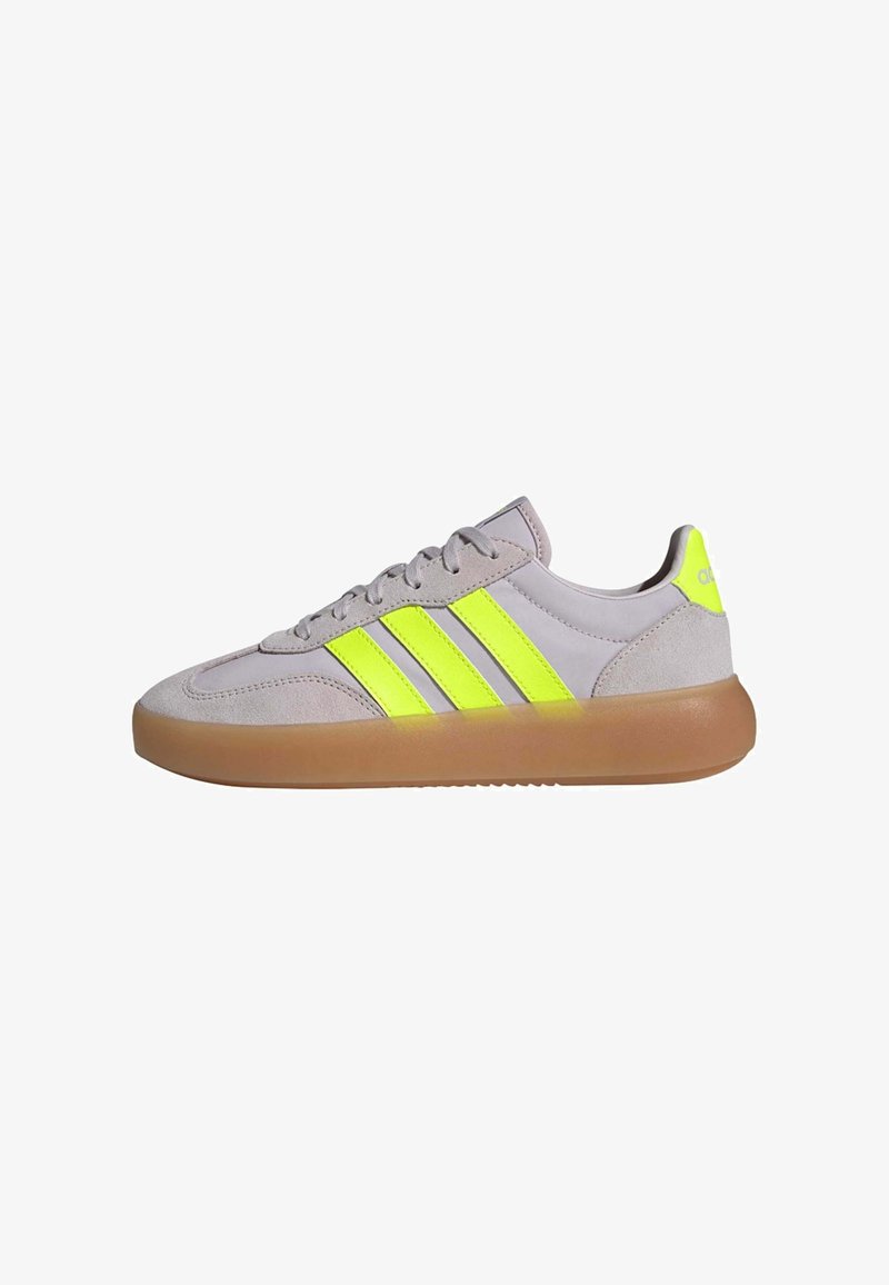 Light grey athletic shoe with yellow accents, featuring three stripes. Soft suede upper, rubber gum sole, and rounded toe design.