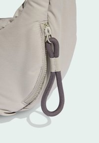 Beige påse med en slät tygfinish, med en synlig dragkedja och en mörklila ögla för enkel hantering.