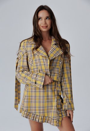 Geel geruite jas met lange mouwen, oversized kraag en golvende zoom. Bevat bruine en blauwe accenten, stofstrikdetail op de taille.
