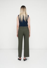 Pantalones de pierna ancha en verde oliva con un ajuste entallado, que cuentan con bolsillos en la parte trasera y una textura de tela suave, combinados con una blusa sin mangas oscura.