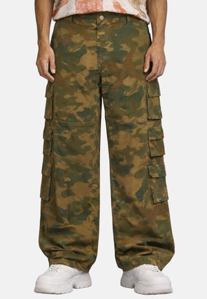 Pantaloni cargo camouflage a vestibilità ampia con multiple tasche laterali, polsini elasticizzati, indossati con sneaker bianche chunky.