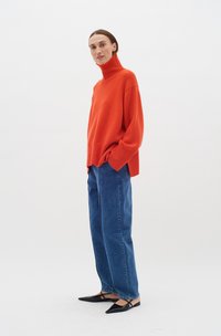 Pulover tricotat portocalie cu guler înalt, croi lejer, asociat cu blugi blue denim cu talie înaltă și pantofi negri cu vârful ascuțit. Textură netedă, design minimalist.